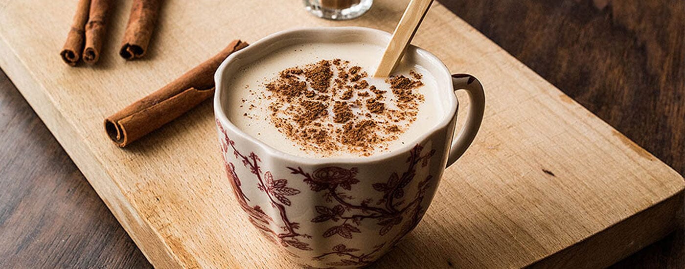 Çiçekli bir fincan içinde lezzetli görüntüsüyle iştah kabartan salep içeceği ve aroma katmak için içine eklenmiş iki parça rulo tarçın