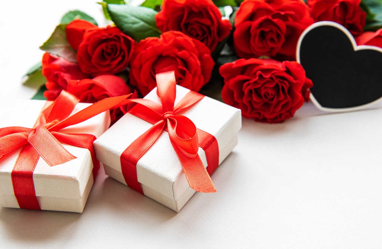 güllerin önüne bırakılmış kırmızı kurdeleye sarılı iki hediye kutusu