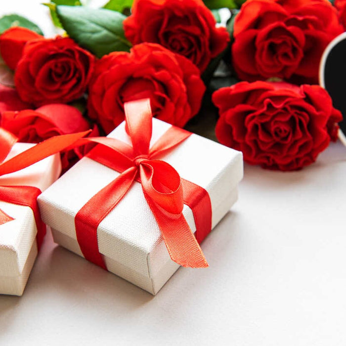 güllerin önüne bırakılmış kırmızı kurdeleye sarılı iki hediye kutusu